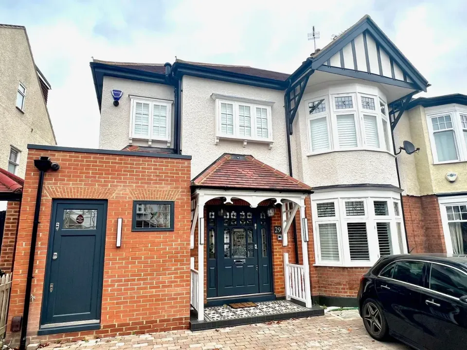 traditional semi detached house with red brick extension, dark front doors, white bay windows and tiled porch roof